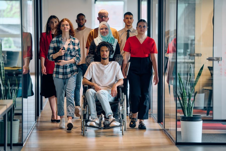 Un groupe de personnes diversifiés entourent une personne en situation de handicap